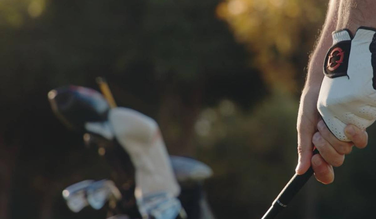 Golfer gripping a golf club with a red EXO Golf Glove. Golf Clubs in the background