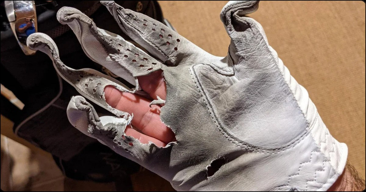 Worn out leather golf glove with torn fingers showing advanced grip degradation after heavy use