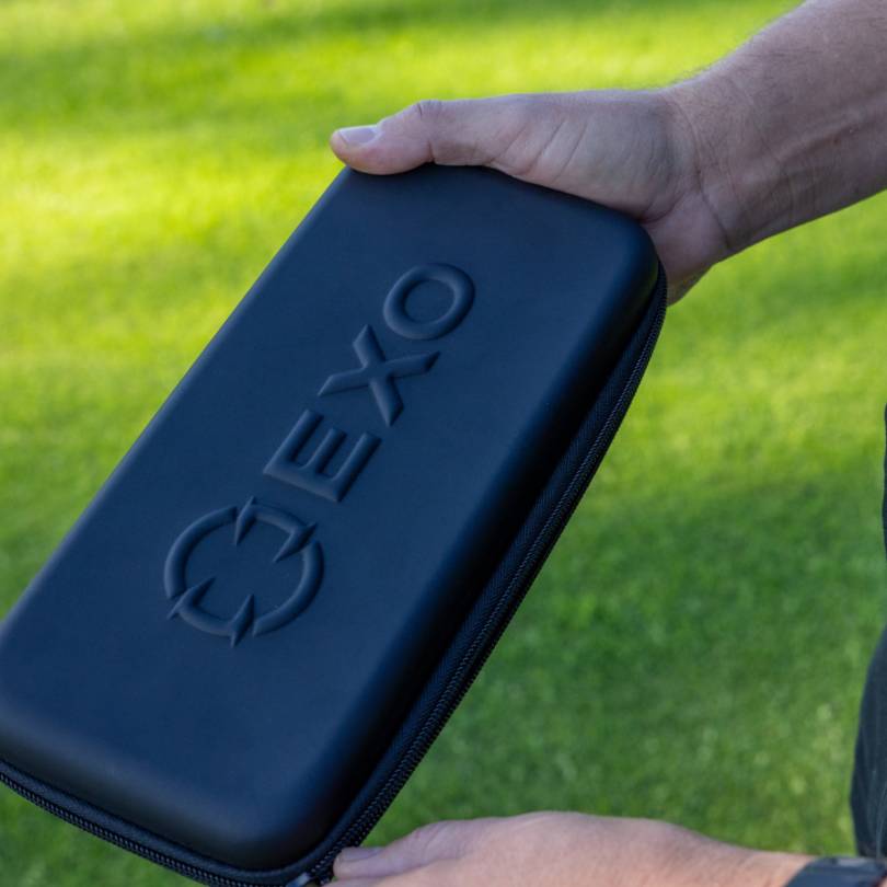 Golfer holding closed EXO Golf glove case - hard shell case closed showing embossed EXO logo on black exterior against grass background