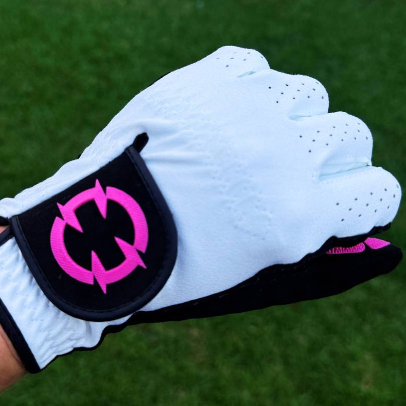 EXO Golf Glove pink colorway back of hand view showing pink EXO logo on wrist strap against grass background