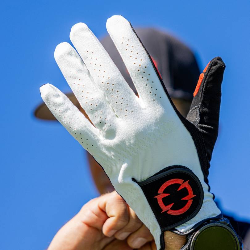 EXO Golf Glove red colorway back of hand held up showing perforated panel and EXO logo on wrist strap against blue sky