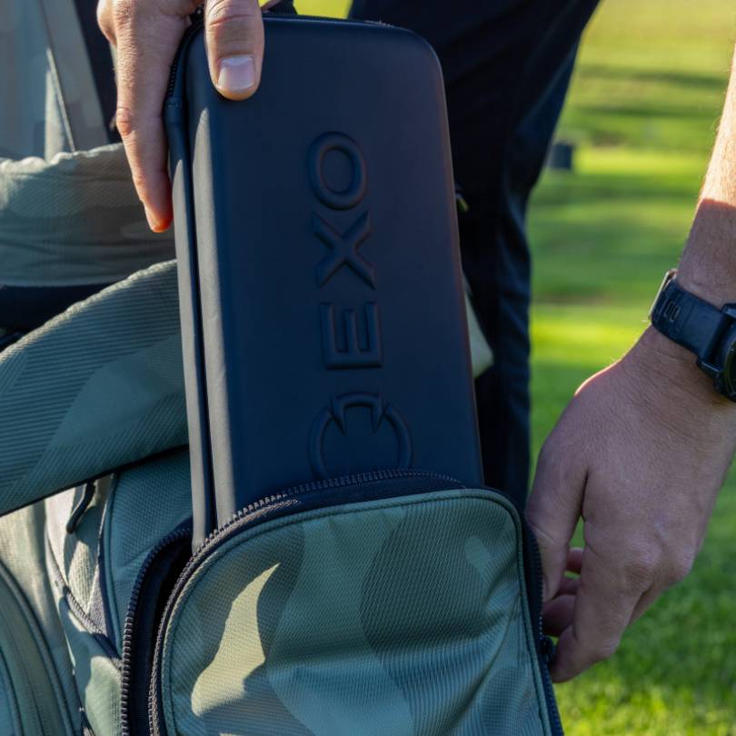 Golfer sliding EXO Golf hard shell glove case into golf bag pocket showing embossed EXO logo on black exterior