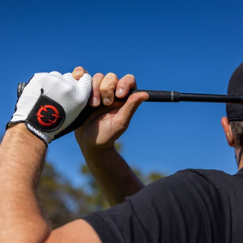Golfer holding finish position wearing EXO Golf Glove red colorway with both hands visible on club against blue sky