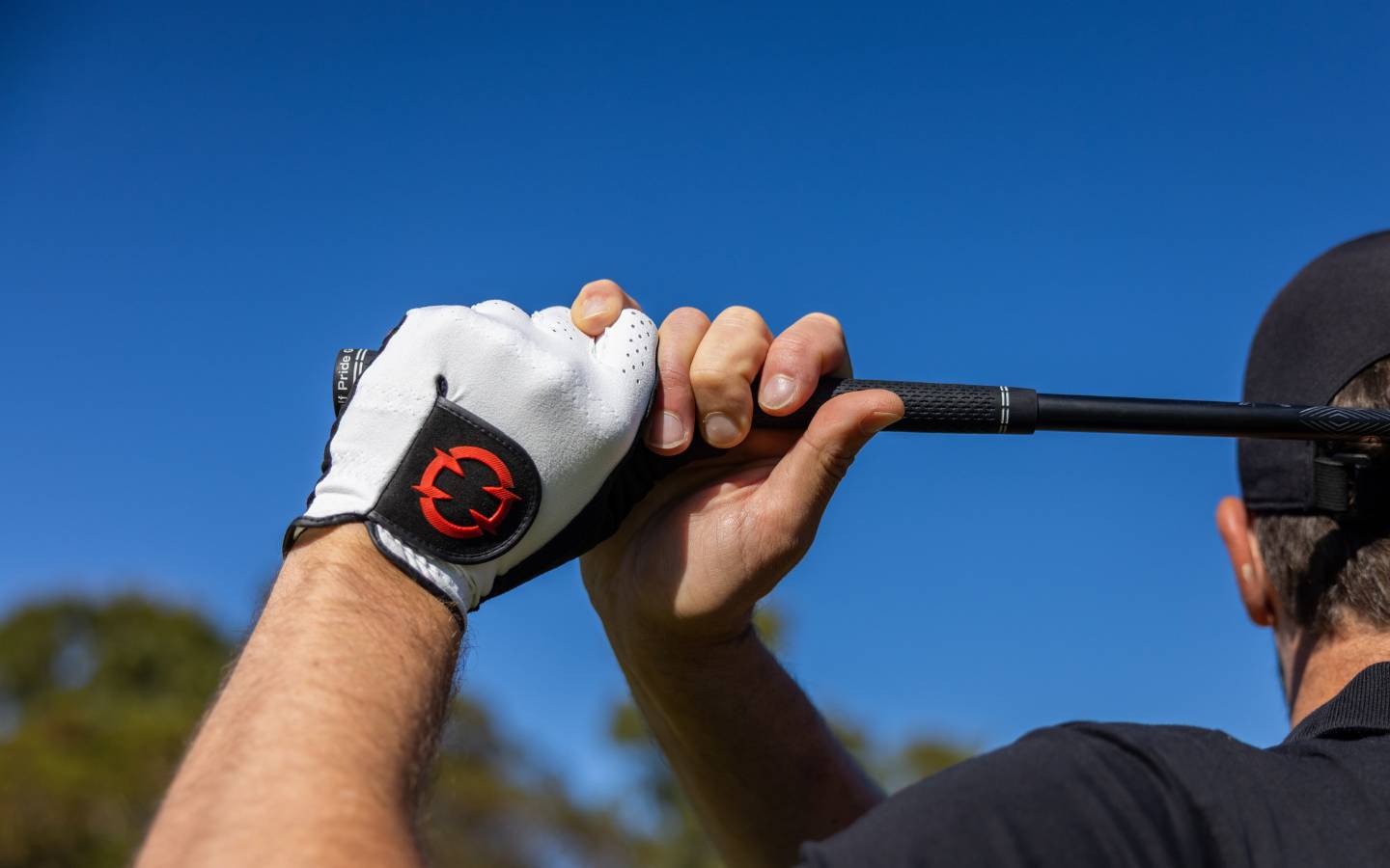 EXO Golf Glove red colorway shown on golfer gripping club at finish position with EXO logo visible on wrist strap